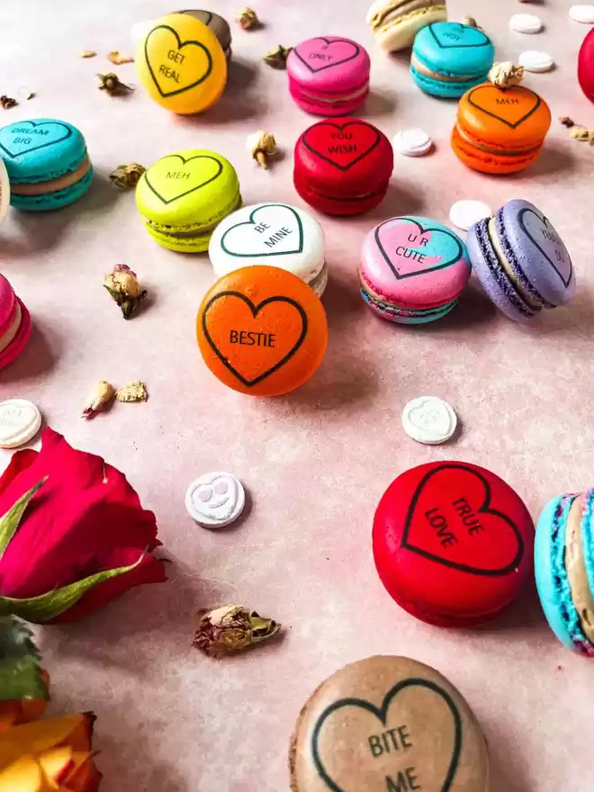 colourful valentine's day macarons, decorated like conversation love heart candy on a pink background with colourful roses
