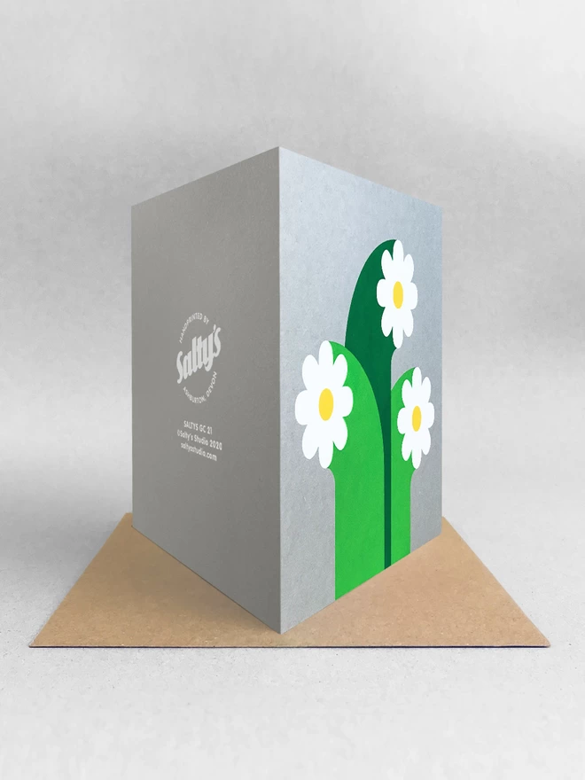 Rear view of a three white flowers card with oversized stems screenprinted on grey square card. Stood on a brown kraft envelope in a light grey set