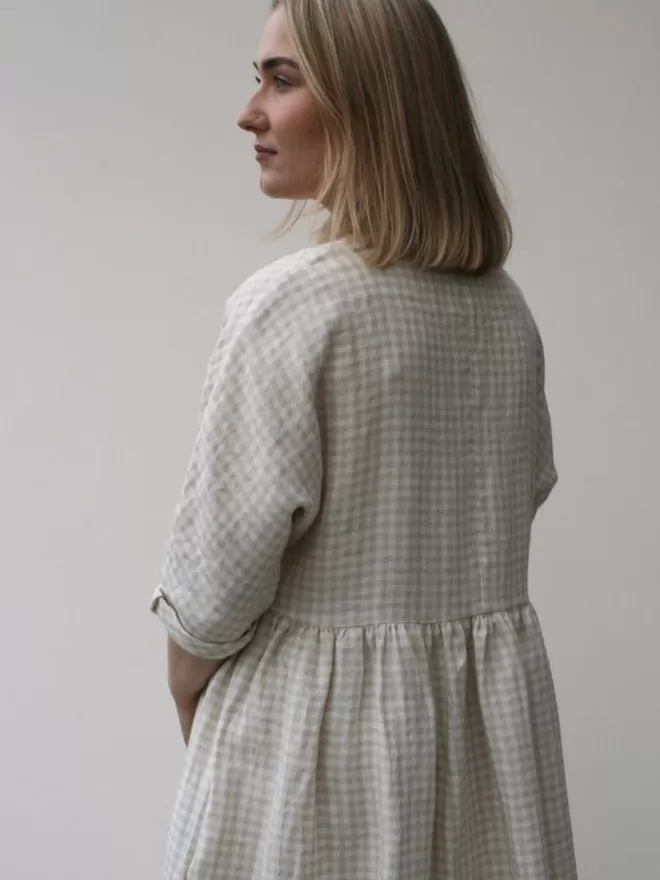 Linen dress in a neutral oatmeal check. Scooped neckline, gathered skirt and elbow length sleeves. Mid calf length and deep side seam pockets.