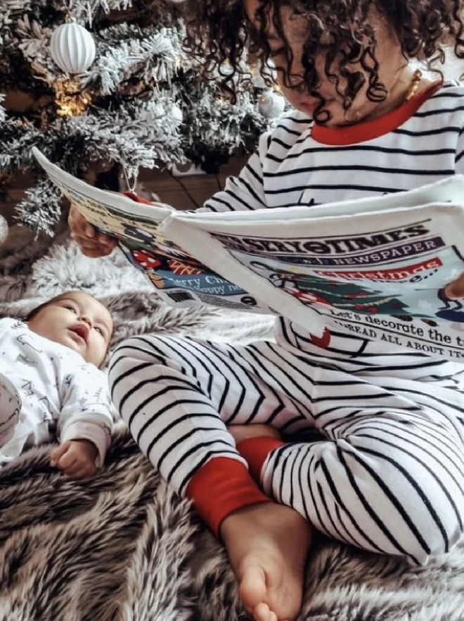 Toddler reading the Christmas is Here newspaper with newborn baby