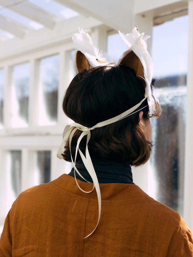 A shot of a woman wearing a luxury wolf mask from the back showing it's ribbon ties tied in a bow