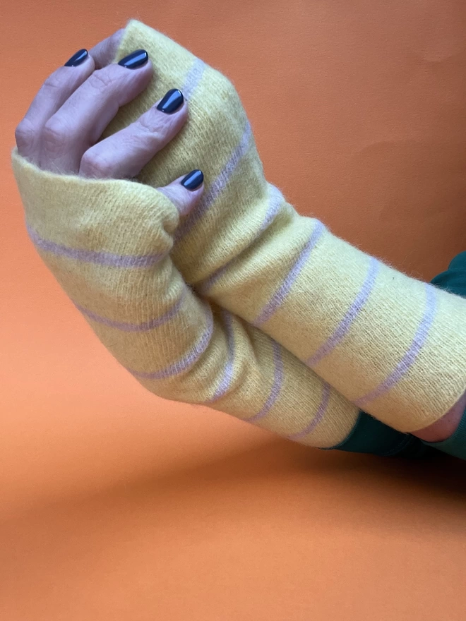 Yellow knitted wristwarmers shown worn with hands ientwined