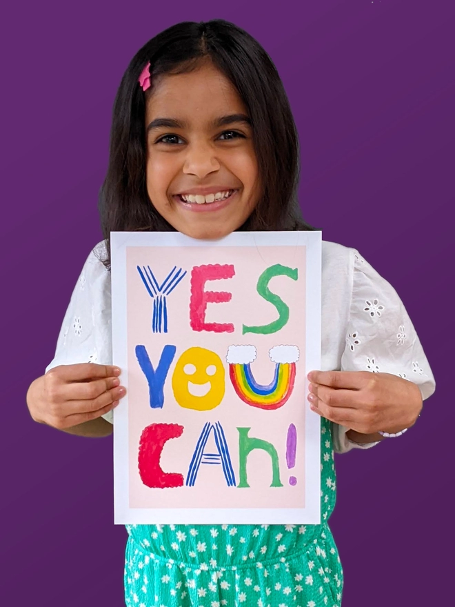 Young girl standing holding an art print saying 'Yes you can'