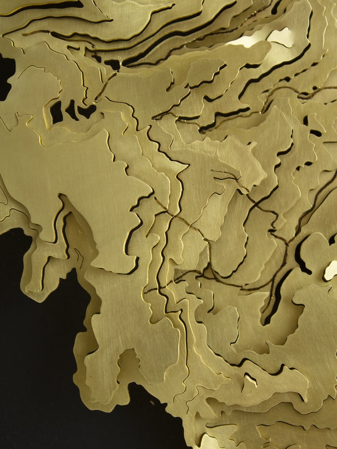 close up of a brass topographical contour map piece, mounted on black.