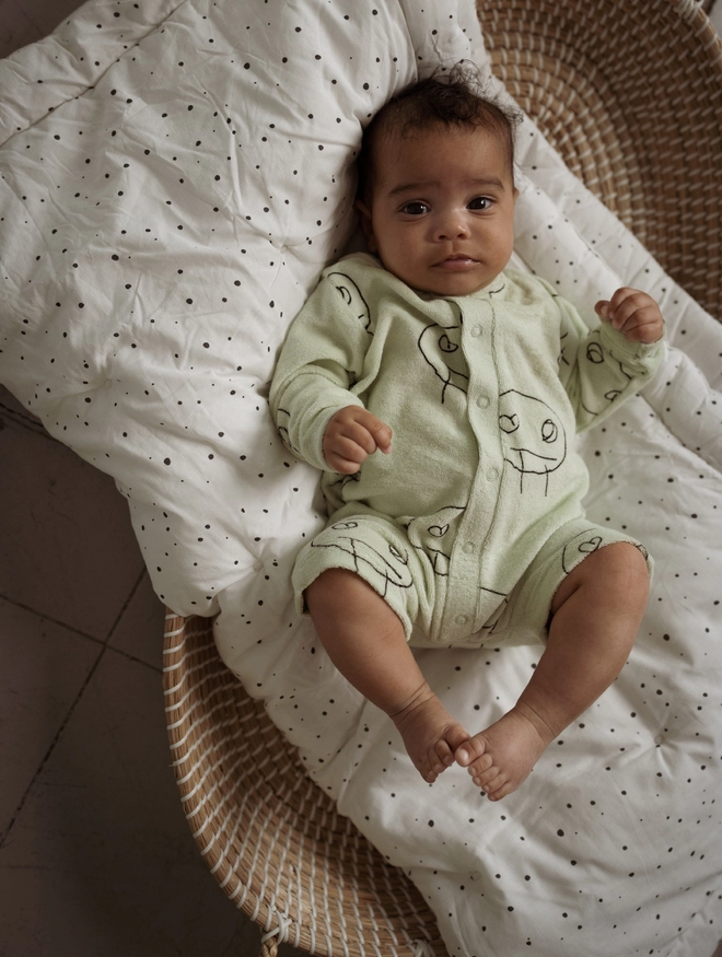 Olive Freds Face Terry Towel Romper seen on a baby lying in a cot.