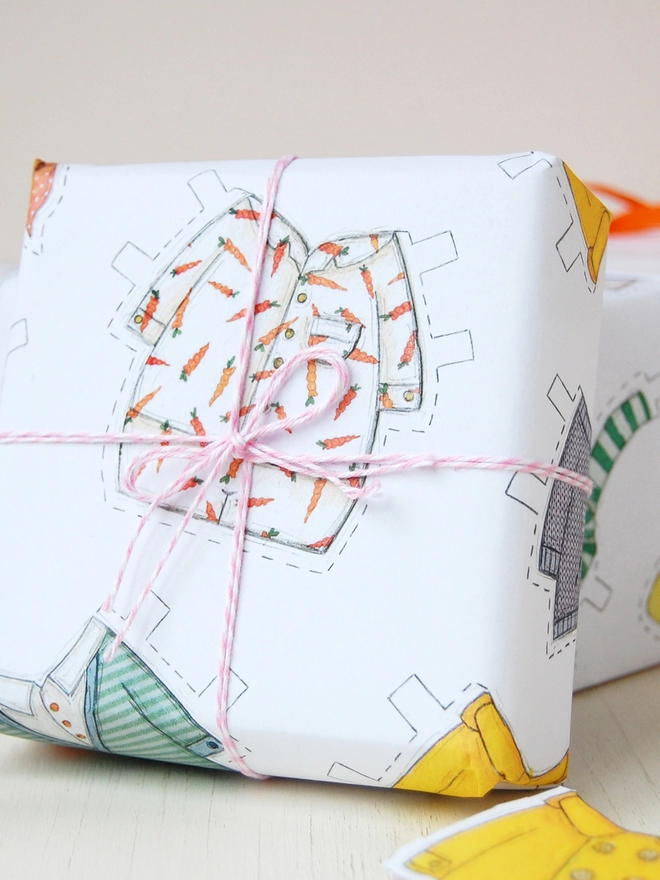 A gift wrapped in white wrapping paper illustrated with paper doll outfits for an Easter bunny.