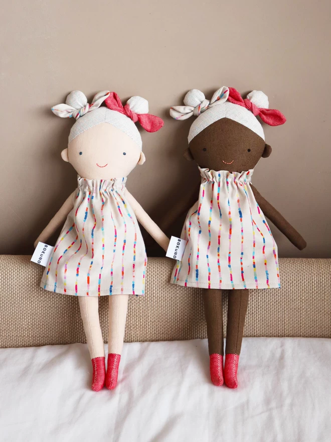 textile girl doll in light and dark skin with rainbow coloured hair and dress