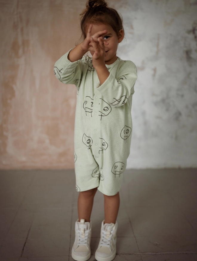 Another Fox Olive Freds Face Terry Towel Romper seen on a child holding their hands up.