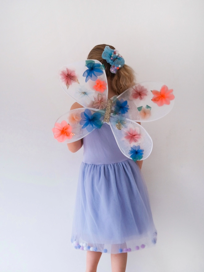 Young girl posing wearing a lilac tulle pom pom filled dress and fairy wings.