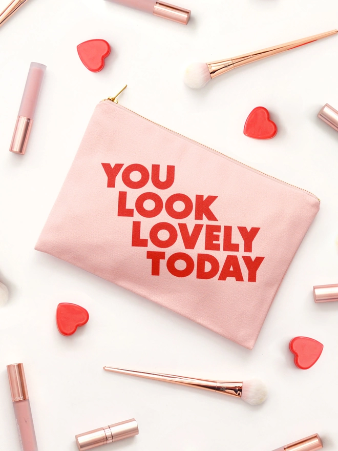 a blush pink canvas zip pouch with the words you look lovely today surrounded by makeup 
