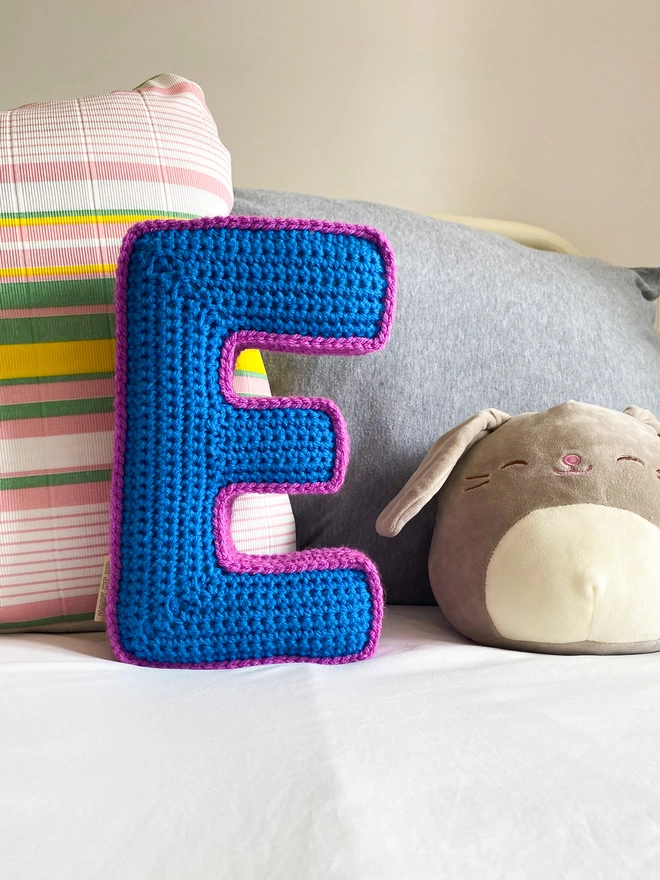 Crocheted Letter E Cushion in Blue & Magenta on child's bed