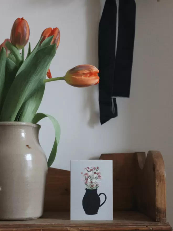 a card with flowers on next to vase of tulips