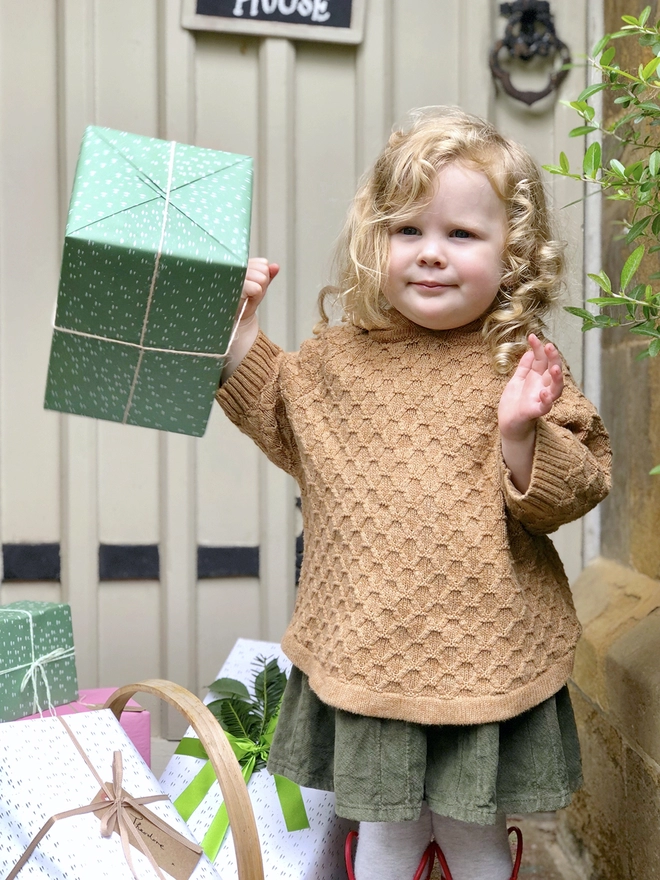 A toddler is holding a gift wrapped in green wrapping paper with a tiny tree design.