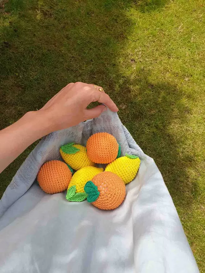 Three crochet oranges and three crochet lemons cradled in blue fabric.