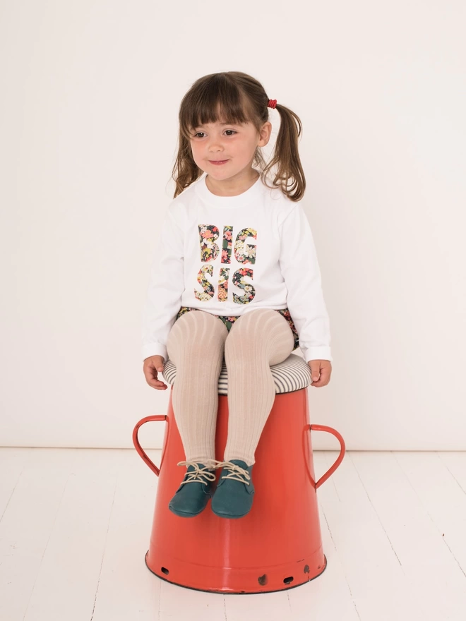 big sis appliquéd on a long sleeve white cotton t-shirt worn by a happy little girl