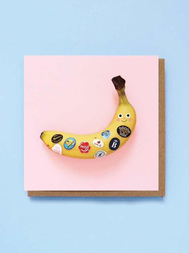 A pink square card with a happy banana with fruit stickers 