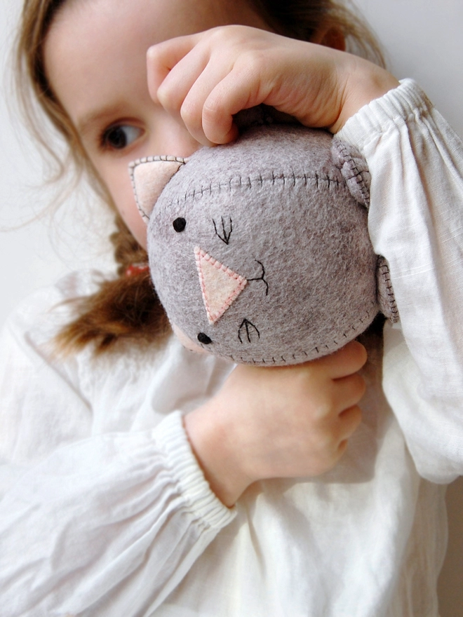 A young girl is holding a handmade grey felt kitten toy.