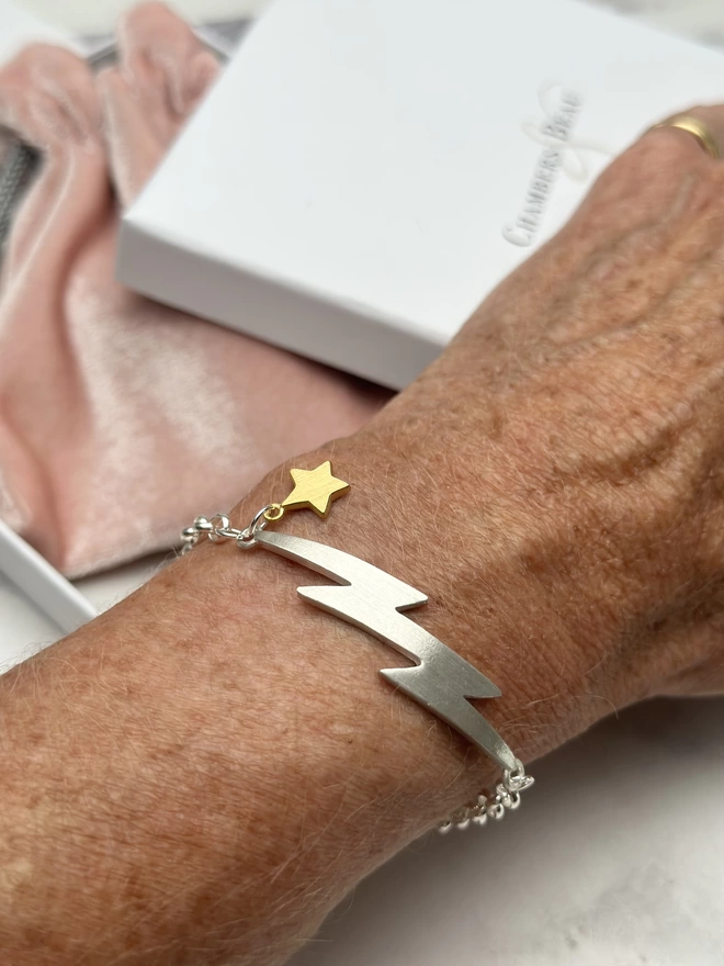 model wears personalised sterling silver electric, lightning bolt charm bracelet on silver belcher chain with small gold plate mini star charm. gift box and pouch