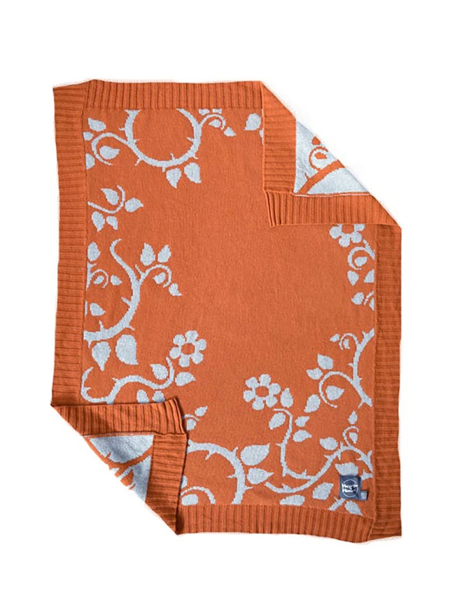 Product shot of the front of the rust briar rose baby blanket, rust orange with trailing blue flower and thorn design.