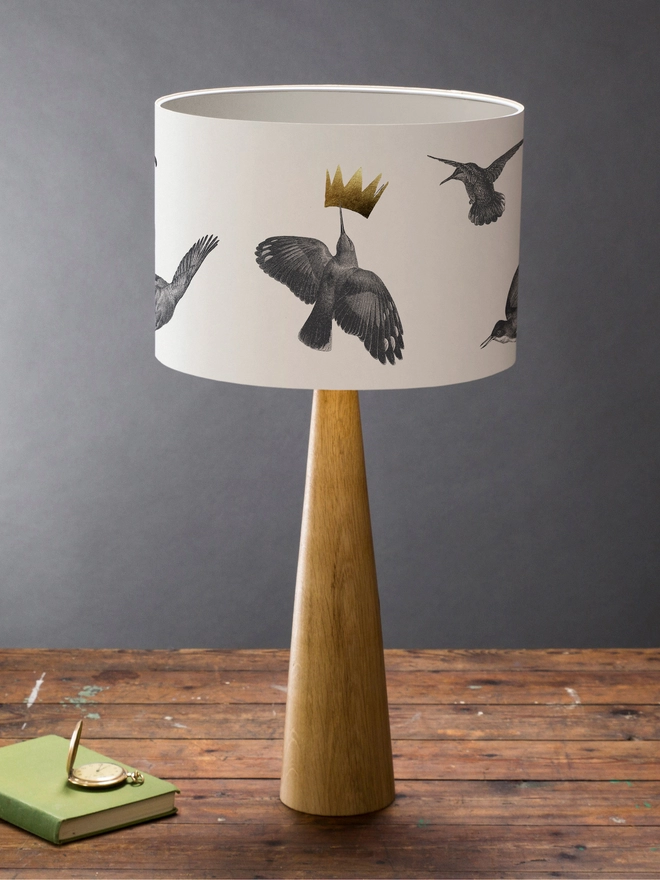 Drum Lampshade featuring hummingbirds on a wooden base on a shelf with books and ornaments