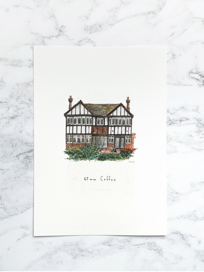 Beautiful watercolour illustration of 65mm Coffee, independent cafe and coffee shop in Tonbridge.  A characterful black and white tudor style two storey building with small diamond paned windows on the ground floor and brick below. There is dark green foliage and bushes infront of the building. The watercolour style is painted with a black pen outline and organic loose style with small details. The print is a small illustration on the centre of a white page and the paper sits on a white marble background.