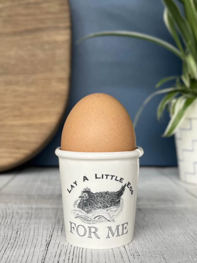 A handmade egg cup, emulating a paper cup, featuring ‘Lay A Little Egg FOR ME’ song lyrics. 