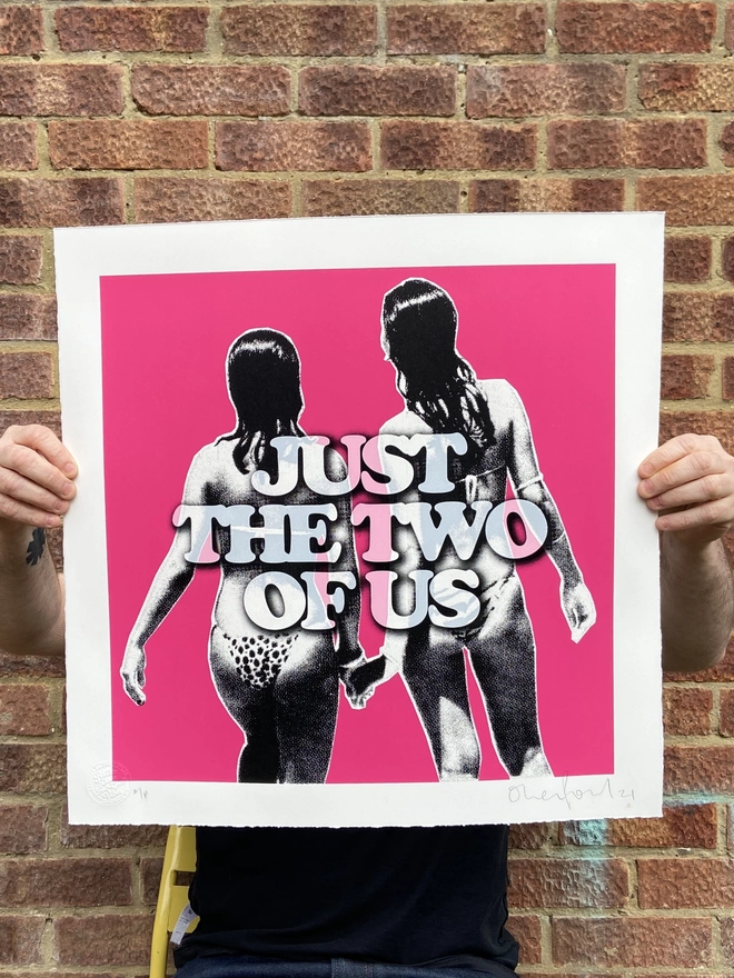 "Just The Two Of Us " Hand Pulled Screenprint with a hand torn deckled edge pink background with two women with their backs to us holding hand and just the two of us printed on top 