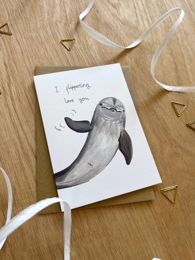 a greetings card featuring an illustration of a dolphin waving its fin with the text “I flippering love you”