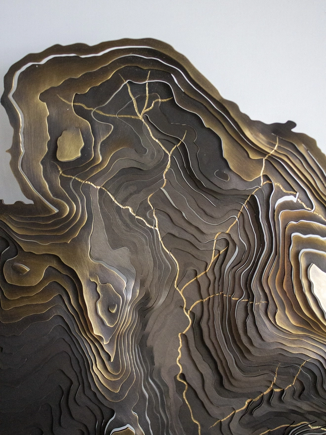 Detail of a blackened brass contour map with engraved golden rivers.