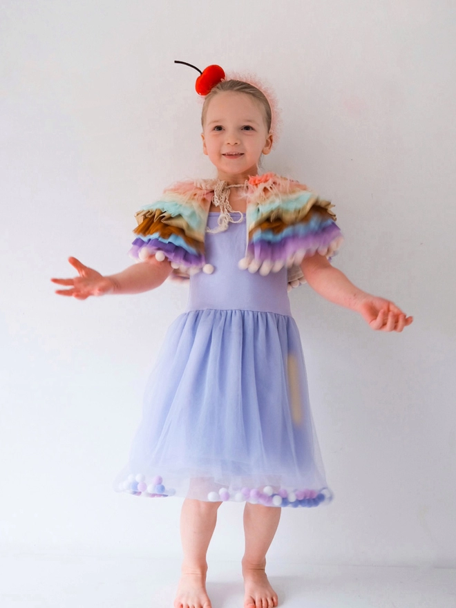 young girl posing wearing a lilac tulle pom pom dress.