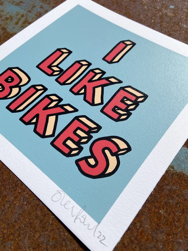"I Like Bikes" Mini Hand Pulled Screen Print square blue background and the words i like bikes hand drawn then printed on top in red letters and a black outline 