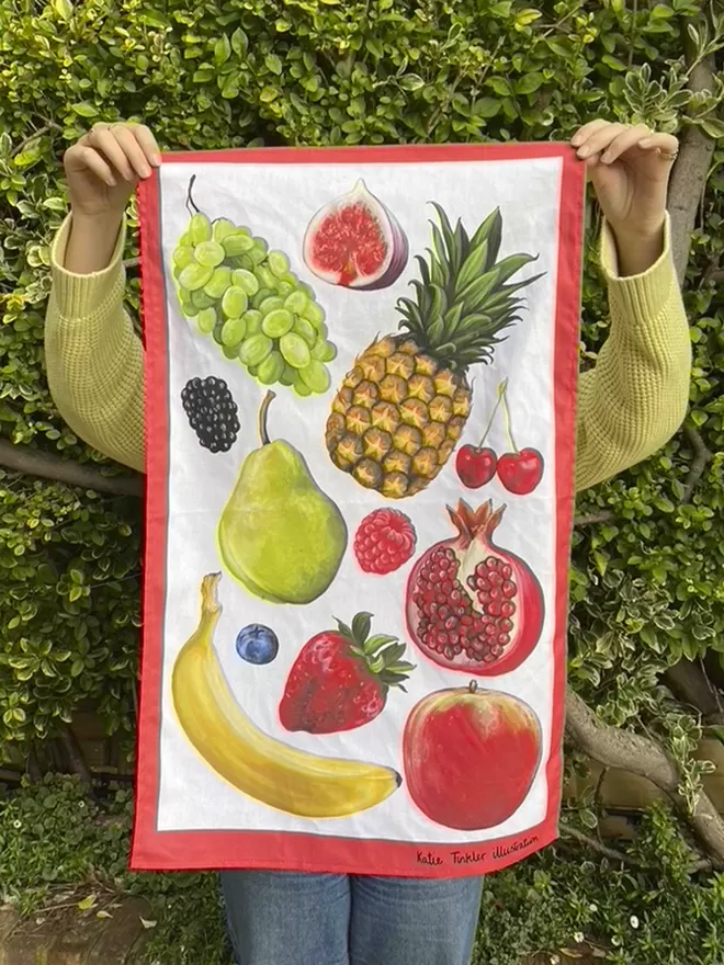 A fruit themed tea towel being held by somebody stood in a garden