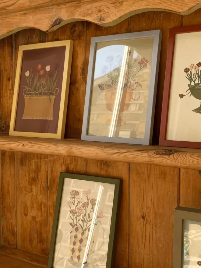 Framed floral prints on a wooden shelf, including Tulips.