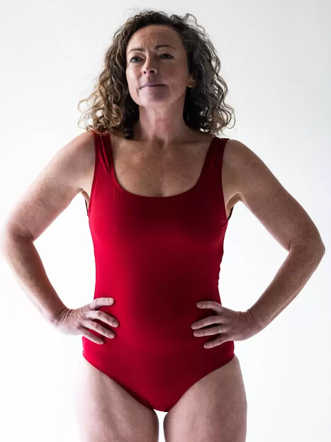 Woman with brown curly hair in studio looking powerful with hands on hips wearing Davy J Sustainable Waterwear red classic crossback swimsuit