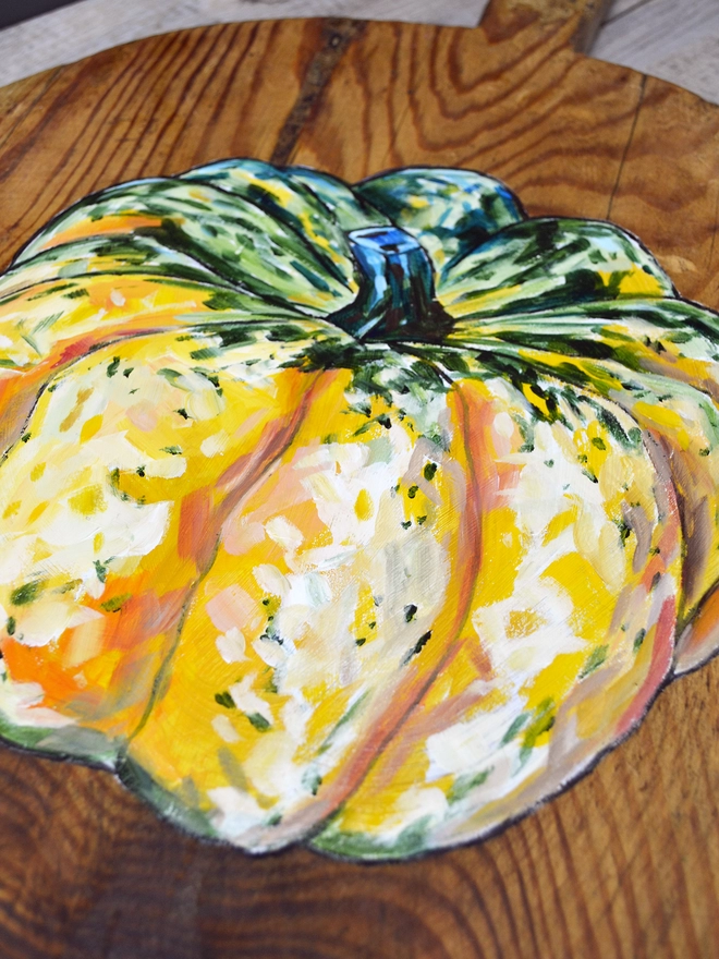 Close up of a wooden chopping board with carnival squash painted design