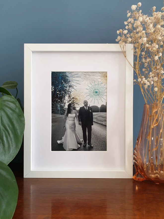 Wedding photo in B&W with hand embroidered sparkly fireworks in white frame on desk
