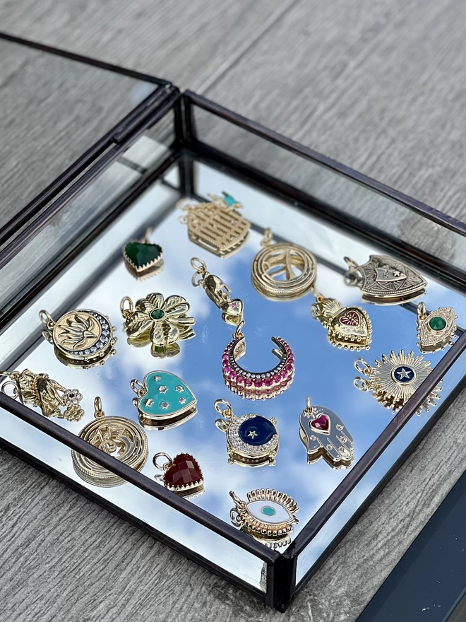 Colourful gold talisman charms in a mirrored jewellery box with blue sky reflecting 