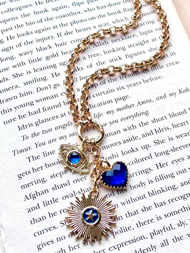 Gold chain necklace with a blue evil eye charm, a blue heart charm and a navy blue star and sunburst charm