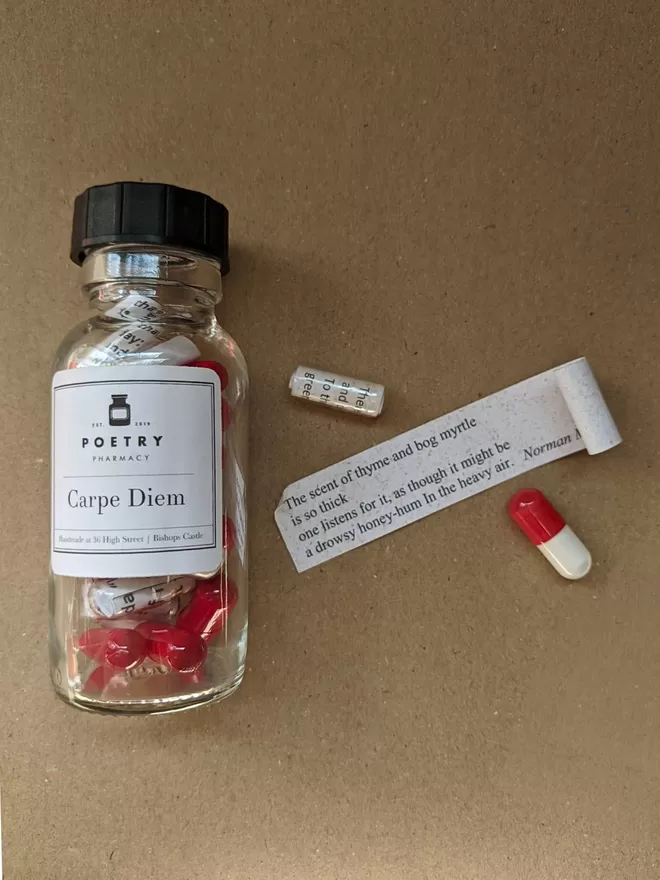 A bottle of red and white Carpe Diem Poetry pills, with one pill open and displaying the quote it contains