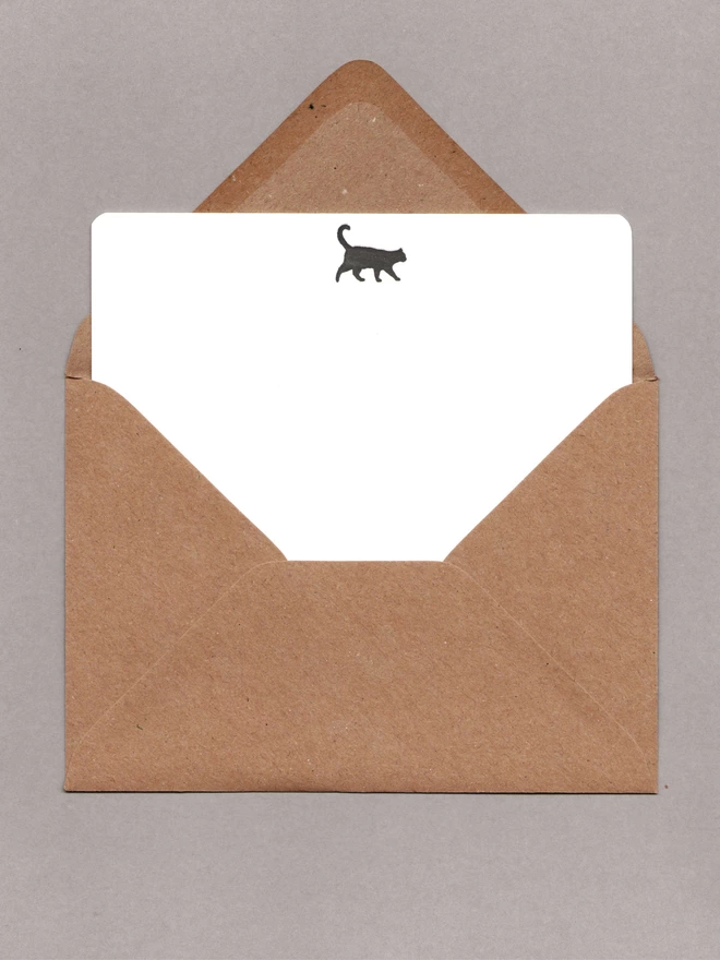 White notecard with a black cat at the top inside an open kraft envelope