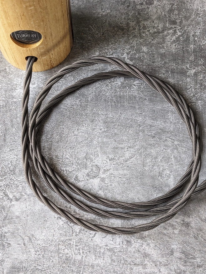 A carefully coiled power cable in twisted elephant grey leading to a UK 3 pin plug in Black.
