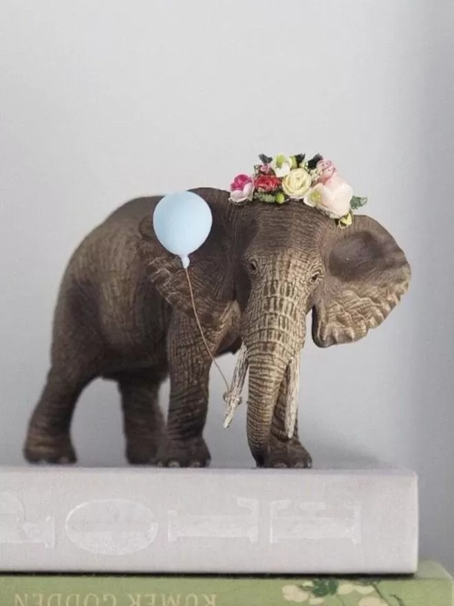 Elephant seen on some books with a floral headdress and a blue balloon.