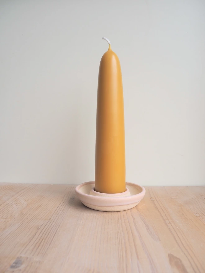 Pale pink candle holder containing a giant stubby beeswax candle on a wooden worktop