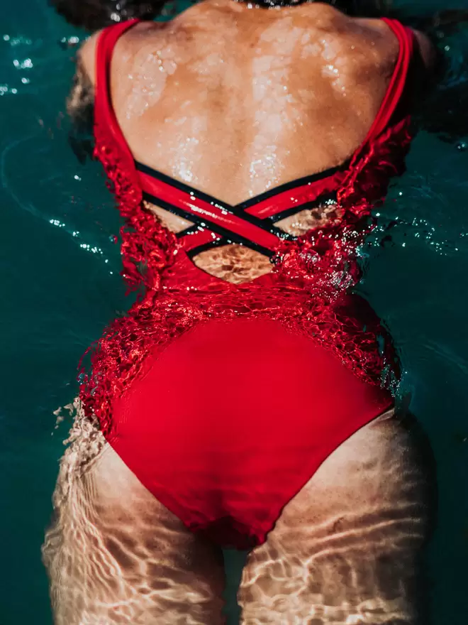 Close up of woman's back as she swims, wearing Davy J Sustainable Waterwear red classic swimsuit with crossback