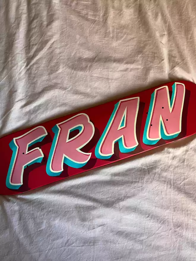 'Fran' painted on a deep pink deck with baby pink lettering, ivory outline and turquoise shade.