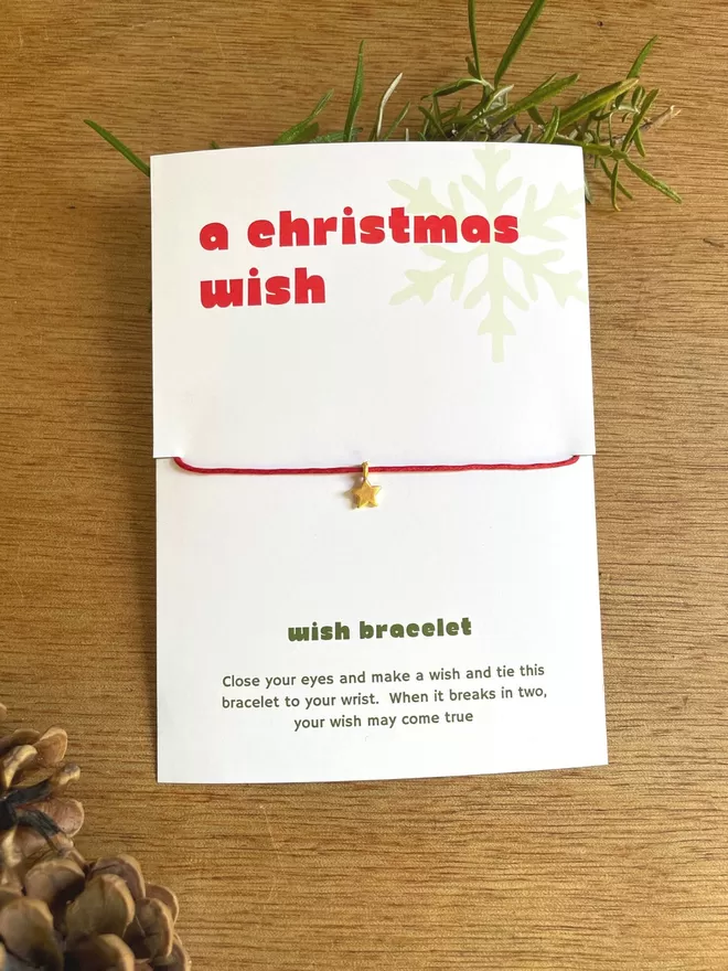 A Christmas Wish bracelet with a red cord and a gold star charm on it's presntation card.