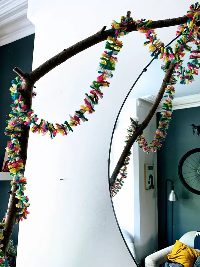Multicolour neon jute string tinsel looped over a branch reflected in a mirror showing a contemporary living room