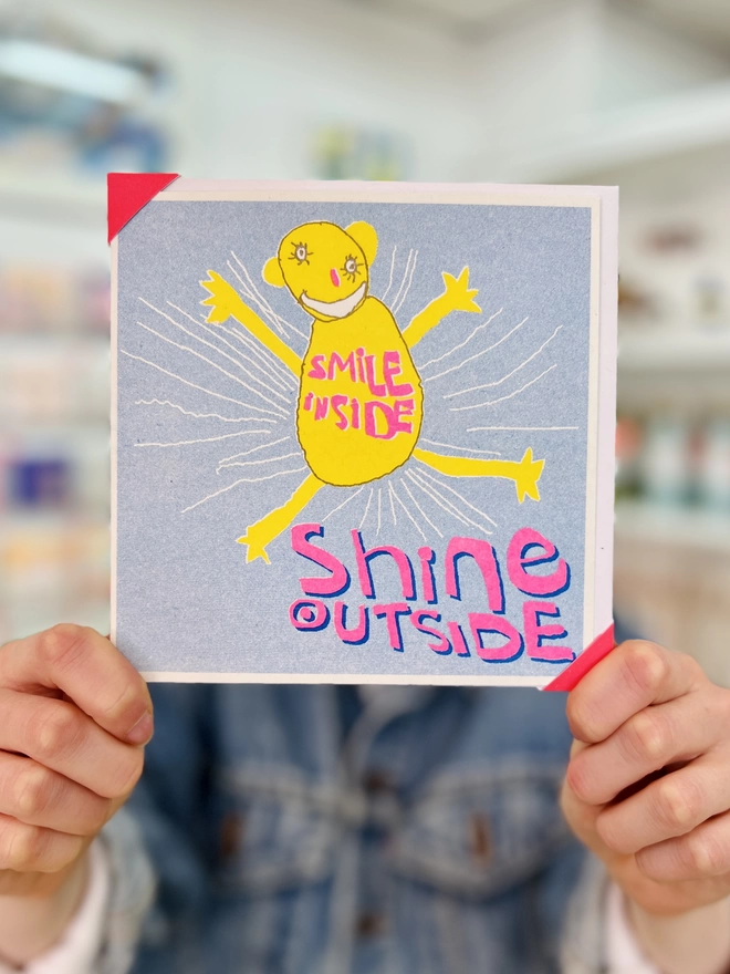 Riso printed encouragement card in blue, yellow and pink with the words Smile Inside Shine Outside