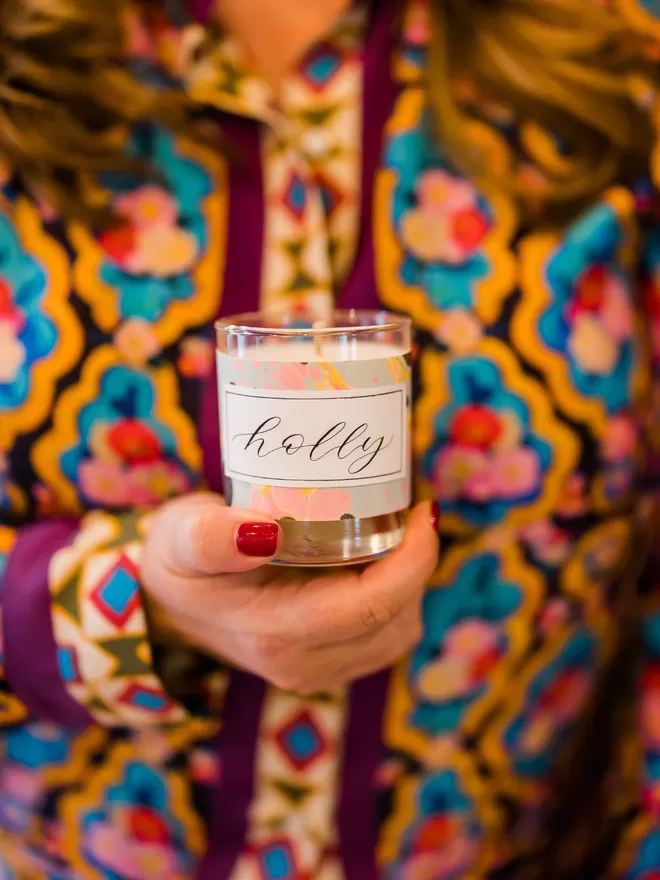 Sassigraphy Hand Poured Scented Candle With Personalised Marbled Label seen held by holly with holly written on the front.