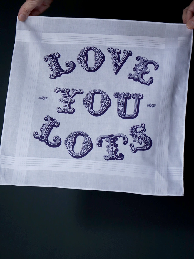 A Mr.PS Love You Lots printed typographic hankie held up against a dark wall